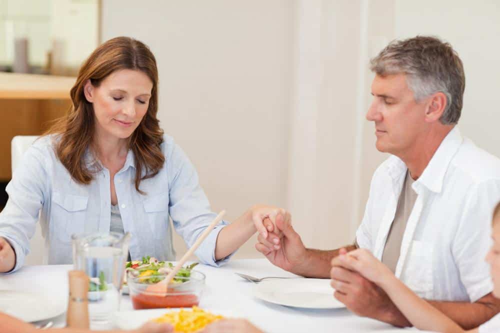 Image of two family members with dinner on the table holiding hands and praying.